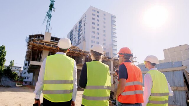 In a safety helmets and goggles group of diverse specialists in the middle with foreman walking down to the construction site and analyzing the plan of the building