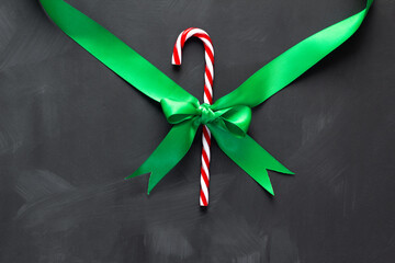 Candy cane tied with a green ribbon on a dark background.