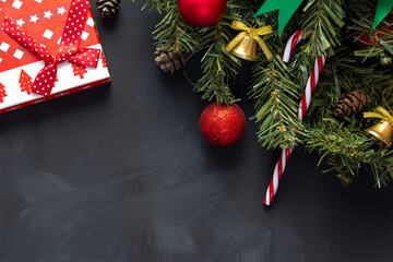 Decorated Christmas tree branch on a black background with red balls and a box with gifts.