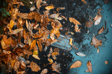 A medical face mask thrown out on the street. The concept of the second wave in the fall, seasonal illnesses, flu, personal protective equipment. Asphalt after an autumn rain