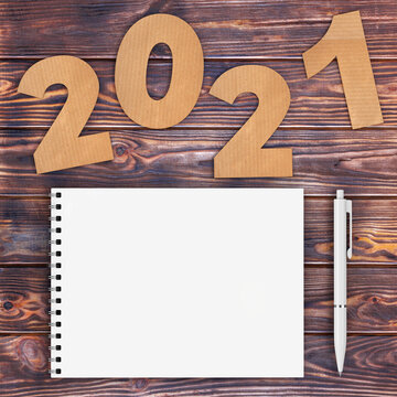 Cardstock Numbers 2021 Happy New Year Sign near White Spiral Paper Cover Notebook with Pen over table. 3d Rendering
