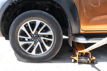 Obraz premium Lift the car with hydraulic floor jack for repairing. Remove wheels to change tires.