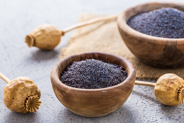 Poppy seeds in small bowl with poppy heads.