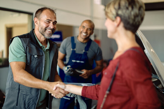 Happy auto repairman handshaking with customer in a workshop.