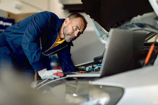 Car mechanic using laptop while examining engine in auto repair shop. - Powered by Adobe