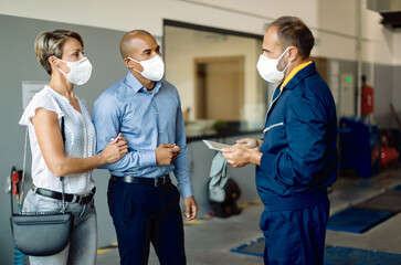 Obraz premium Couple and auto repairman wearing protective face masks while talking in a workshop.