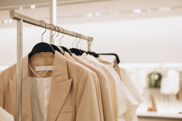 Women's clothes in beige colors on open hangers in store. Selective focus, copy space
