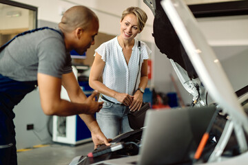 Happy woman talking to her car mechanic in a repair shop.