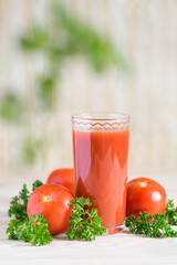 Fresh tomato juice in glass with parsley and ripe tomatoes on light wooden table. Selective focus