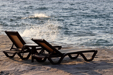 Two empty deck chairs on a stone beach on storm sea background. Beach vacation, quarantine during covid-19 coronavirus pandemic