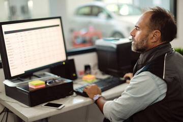 Male foreman working on desktop PC in auto repair office.