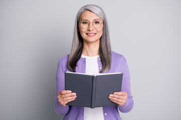 Photo portrait of elder female professor keeping holding a book smiling wearing eyeglasses purple cardigan isolated on grey color background
