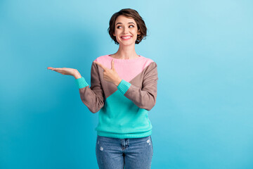 Photo portrait of happy smiling girl pointing finger demonstrating holding in hand blank space isolated on pastel light blue colored background