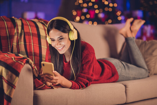 Photo Portrait Of Woman Laying On Couch Holding Phone In Two Hands With Earphones Indoors