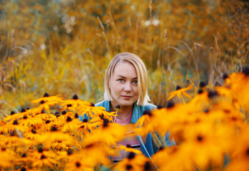 Beautiful blonde woman sitting at flower meadow in autumn forest. Fall season outdoor colorful portrait