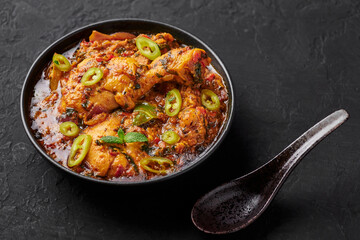 A Chicken Patiala in black bowl on dark slate table top. Murg Patiala is indian cuisine curry dish with chicken meat, spices, curd and cashew nut paste. Asian food and meal.