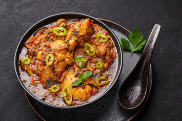 A Chicken Patiala in black bowl on dark slate table top. Murg Patiala is indian cuisine curry dish with chicken meat, spices, curd and cashew nut paste. Asian food and meal.