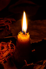 Close up of a bee wax candle surrounded by dried leaves  in the dark