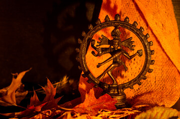 Close-up of a copper figurine of Shiva surrounded by autumn leaves and a orange scarf