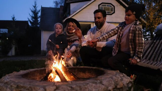 Portrait of a happy American family. They sit around the fire and roast marshmallows