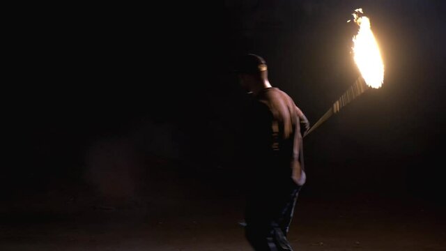 The man twists a long rope with a flame at the end and throws it. Fire show
