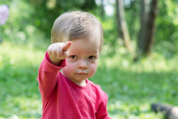 Child in a red shirt looks sternly at the camera and points an imperious finger.