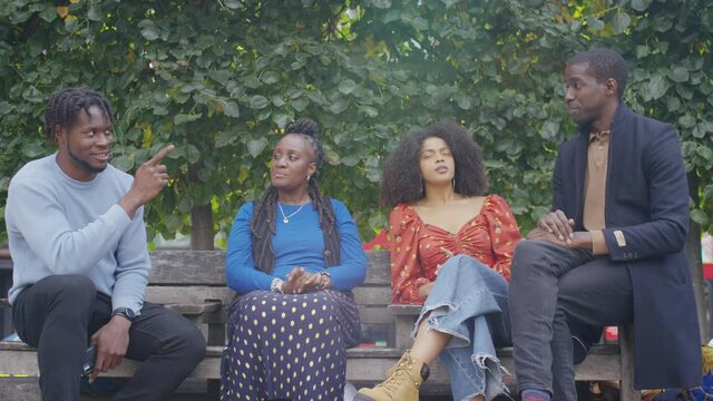 Group of black friends or colleagues sat on a bench outdoors in conversation