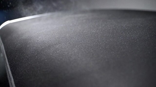 A hand holding a spray bottle, spraying dense white-foamed detergent on a velure car surface, cleaning and disinfencting it, slow motion close up FHD shot.