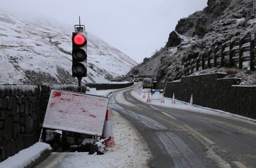 A view of a red traffic light on a snowy, narrow road crossing a bleak, cold mountain pass in...