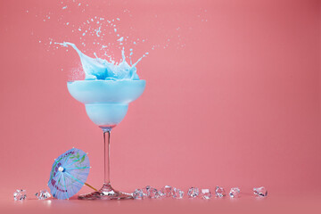 splashing blue drink, cocktail umbrella and ice cubes isolated on a pink background with space for text