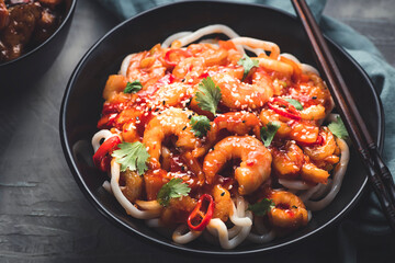 Japanese udon noodles fried with sweet and sour shrimps sauce with hot pepper in asian style, black dishware, concrete background, close up