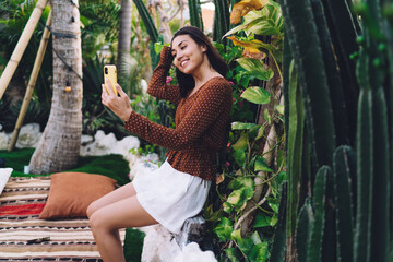 Happy young ethnic female tourist taking selfie in exotic park