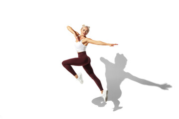 Fototapeta na wymiar Flying like butterfly. Beautiful young female athlete practicing on white studio background, portrait with shadow. Sportive fit model in motion, action. Body building, healthy lifestyle, style concept