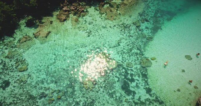 Top down sun reflecting and sparkling at emerald salt water lake. People swim and play in shallow tropical lagoon with crystal clean water. Serene relax for summer vacation of Sumba Island, Indonesia