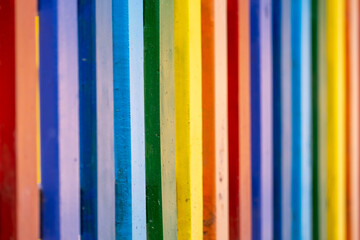 Part of wooden, rainbow colorful painted fence  on a sunny hot summer day in a city park. Abstract vivid multicolored background.