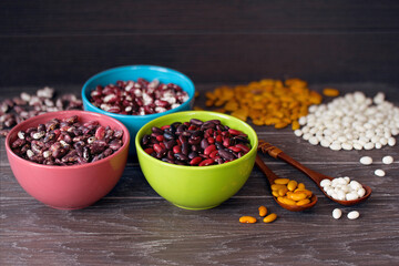 different types of beans in colored bowls and on a wooden table close-up. bean mix close-up in bowls. background with raw colored beans.