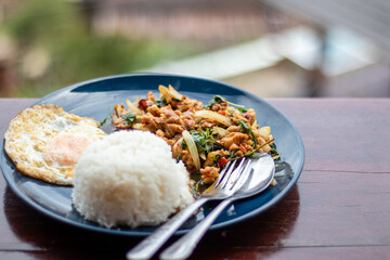 Basil chicken with rice and fried egg in blue plate on wooden table.