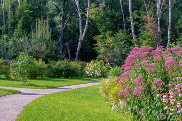Alley in the Park with flowers and trees around. The road goes into a grove of trees.