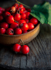 Hawthorn in a wooden bowl on the table. A medicinal plant similar to the wild rose. Still life with place for text. Harvest. Copy space.