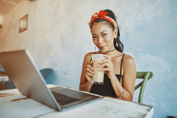 a young mixed race woman drink iced coffee and using her laptop in cafe