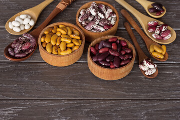 different types of beans in wooden bowls and wooden spoons on a wooden table close-up. bean mix close-up in bowls. background with raw colored beans.