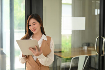 Fototapeta premium Portrait of an attractive young woman holding her digital tablet while working in modern office.