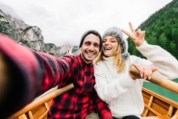 Romantic couple of adults in love taking a selfie on a boat visiting an alpine lake at Braies Italy at autumn fall. Couple, wanderlust and travel concept. Cold colours.