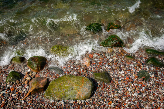 Summertime closeup of stones, pebbles and fresh water on a rock beach.