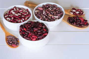 different types of beans in white bowls and wooden spoons on a white background close-up. bean mix close-up in bowls. background with raw colored beans.