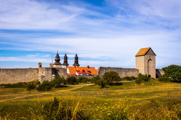 Naklejka na ściany i meble Beautiful rural summer view of an ancient medieval brick tower and defense wall surrounding the city of Visby Gotland, Sweden. Blue sky and grassy fields.