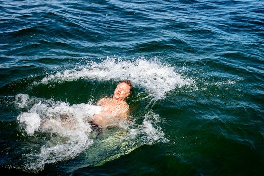 Caucasian male with painful facial crinch expression jumps backwards into icy splashing water in the ocean of the Baltic Sea.