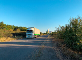 Fototapeta na wymiar White truck driving on a road at sunset coming from thermal power plant in distant