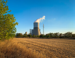 Fototapeta na wymiar Cooling tower of thermal power plant behind plowed field in autumn dusk