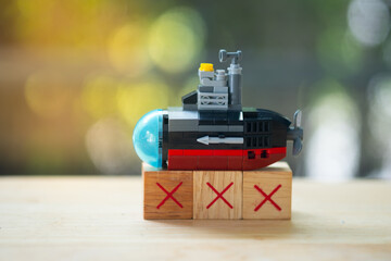 Plastic submarine toy placed on X symbol wooden blocks and natural background